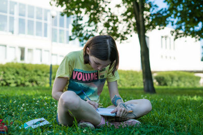 Full length of young woman sketching on book while sitting at park