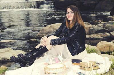 Portrait of young woman with cake sitting by lake