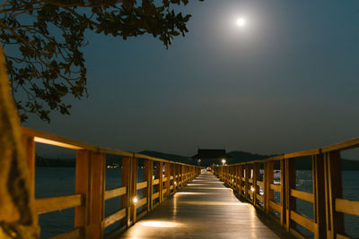 Illuminated footpath amidst trees against sky at night