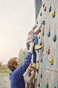 Girl climbing on a wall supported by parents