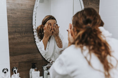 Woman washing her face in front of mirror