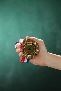 Cropped hand of woman holding medal against wall