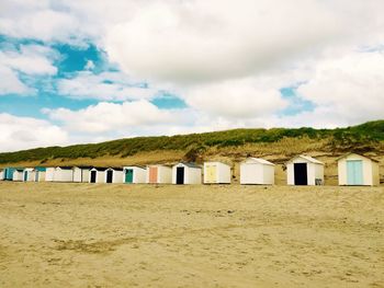 Row of beach huts on sand against cloudy sky