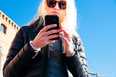 Low angle view of woman using phone against clear sky