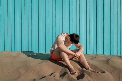 Young man with his head down laughing in the beach in a turquoise wall