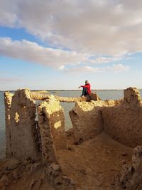 People sitting on rock by sea against sky