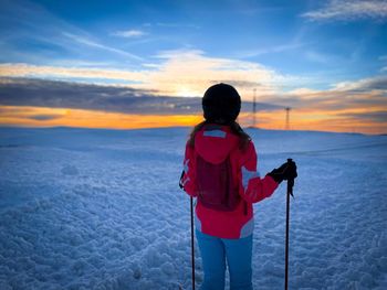 Rear view of boy standing on snow covered landscape during sunset