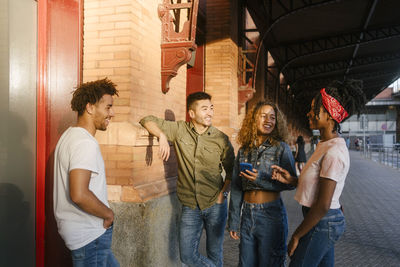 Smiling multiracial friends looking at woman talking on footpath