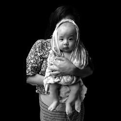 Mother holding baby girls while standing against black background