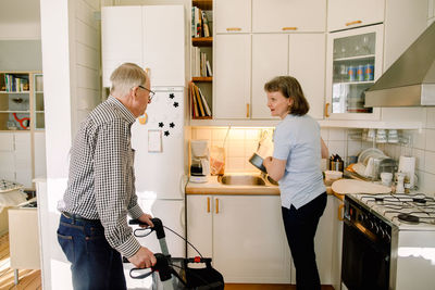 Retired senior man talking to female volunteer washing dishes in kitchen at nursing home
