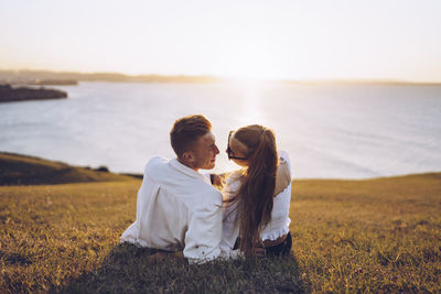 Rear view of couple sitting on sea shore against sky