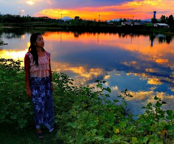Woman standing by lake against sky during sunset