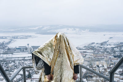 Person covered in golden paper standing against cityscape