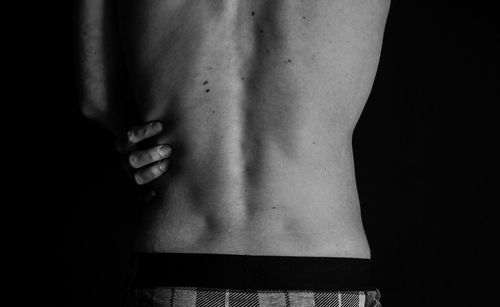 Rear view of shirtless person standing against black background