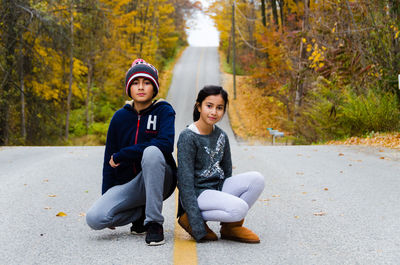 Portrait of smiling siblings crouching on road during autumn