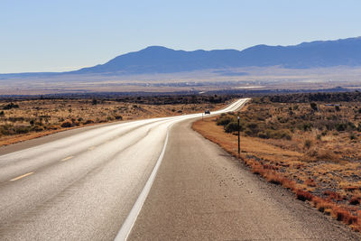 Road leading towards mountains against clear sky