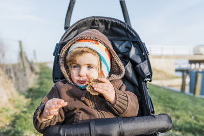 Cute baby girl eating cookie while sitting in stroller
