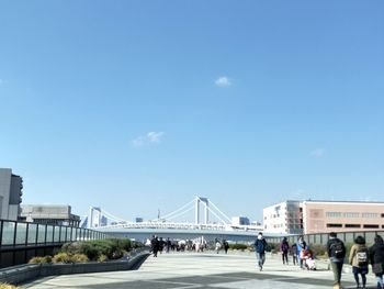 People on bridge in city against blue sky