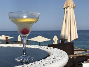 Glass of water on table by sea against sky