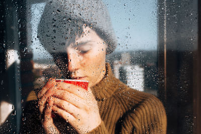 Portrait of woman seen through wet window in rainy season