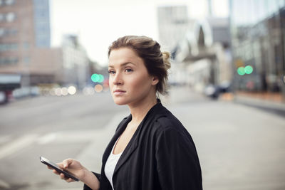 Woman holding mobile phone while standing in city