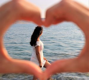 Cropped hands making heart shape in front of woman looking at sea