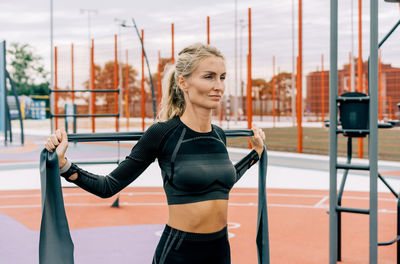 Young athletic woman is training on the sports ground using sports elastic bands.