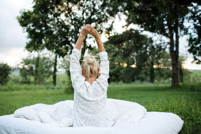 Young blonde woman wake up wear pajamas sitting in bed on white blanket outdoors over nature