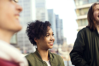 Smiling teenager with short hair standing amidst friends in city