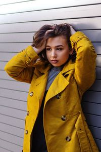 Portrait of young woman standing against yellow wall