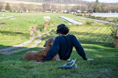 Golden retriever dog and young man sit together on a grassy farmland hill