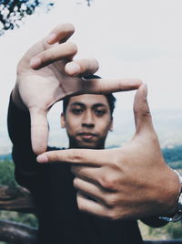 Close-up of young man gesturing finger frame against sky