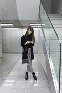 Full length of woman using mobile phone on staircase