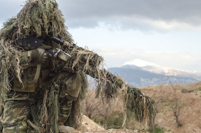 Army man in ghillie suit with rifle on field