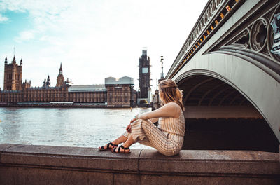 Woman sitting on bridge over river