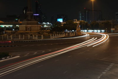 Light trails on road by illuminated buildings in city at night