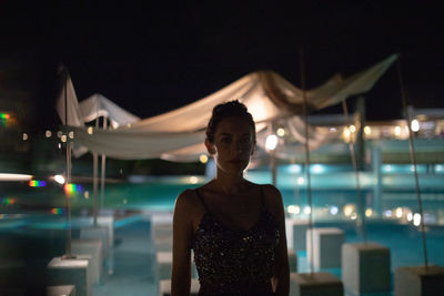 Portrait of woman standing against illuminated restaurant at night