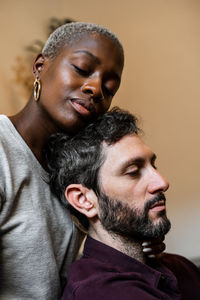 Young bearded man in casual shirt lying on comfortable couch in embrace with african american woman in cozy living room with closed eyes