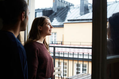 Smiling woman with friends looking through window while standing in rental apartment