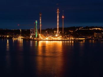 Illuminated buildings by river against sky at night