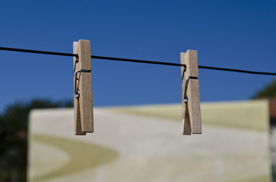 Low angle view of clothespins hanging on rope against clear blue sky