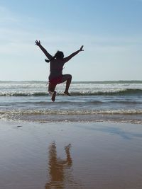 Man jumping on beach against sky