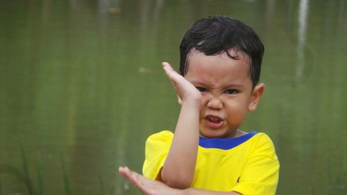 Portrait of boy making face while gesturing against lake