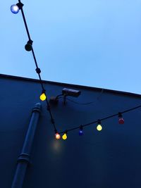 Low angle view of illuminated light bulbs hanging against sky