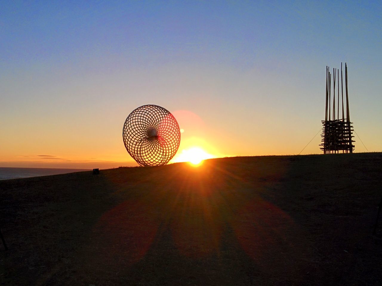 sunset, sun, silhouette, clear sky, orange color, copy space, sky, scenics, tranquility, beauty in nature, tranquil scene, nature, ferris wheel, sunlight, circle, outdoors, low angle view, amusement park, lens flare, idyllic