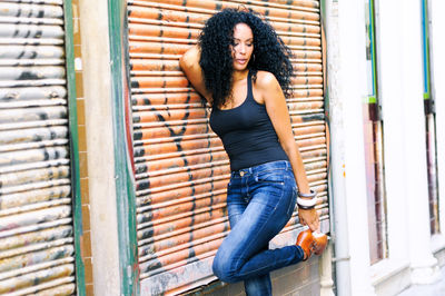 Young woman with curly hair leaning on closed shutter