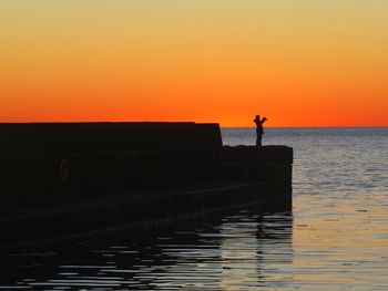 Silhouette man standing by sea against orange sky