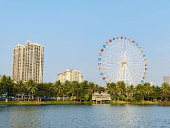 Ferris wheel by river and buildings against sky