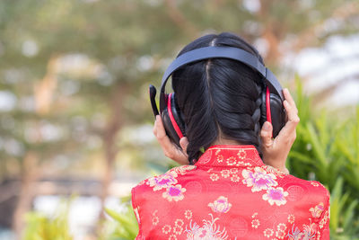Rear view of woman listening music through headphones in park