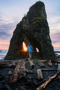 Man walking on log at the beach during sunset near dramatic rock